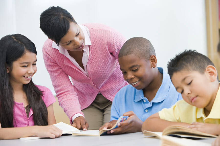 Students in class reading with teacher helping (selective focus)